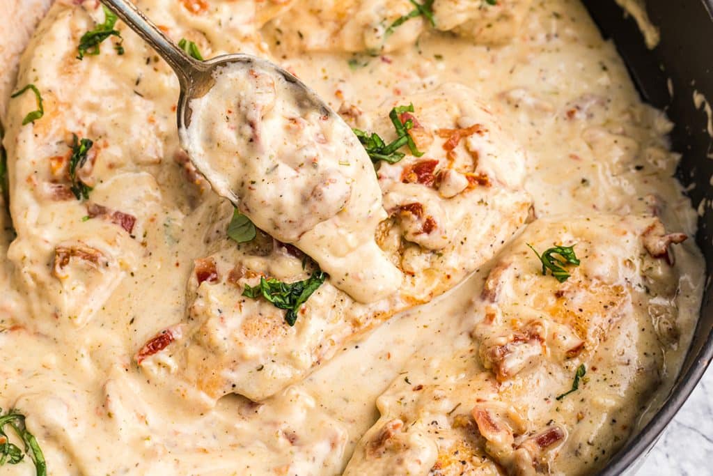 spooning sauce over creamy tuscan chicken