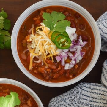 bowl of turkey chili with vegetables topped with cheese, sour cream, and red onion