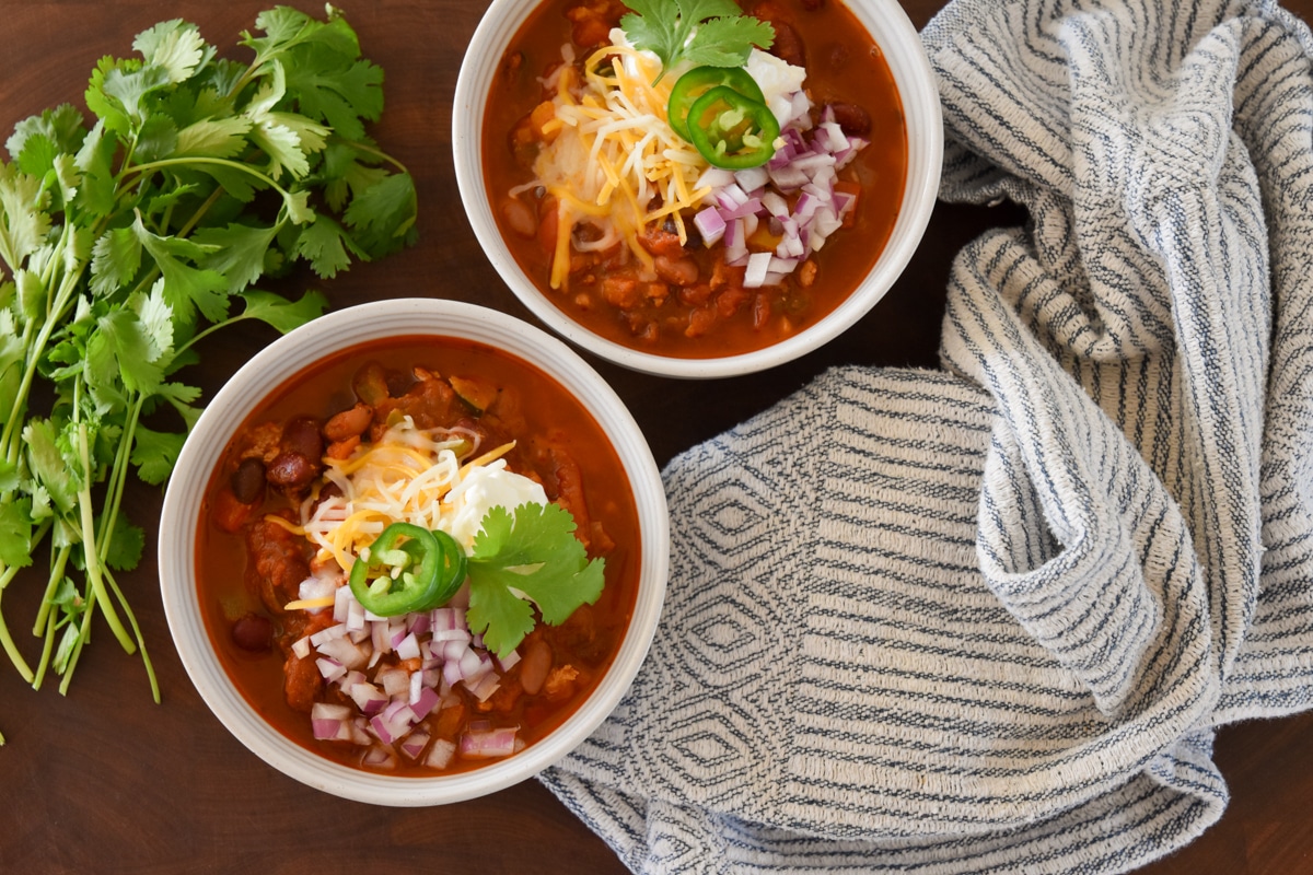 Two bowls of Turkey Chili with Vegetables and all the fixings and a bunch of cilantro.