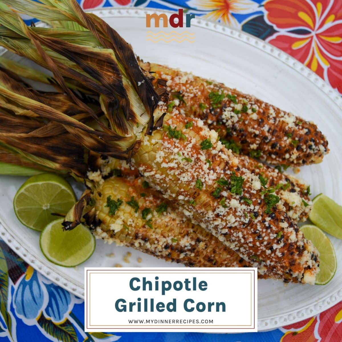 Ears of chipotle grilled corn on white platter with limes wedges on colorful tablecloth. 