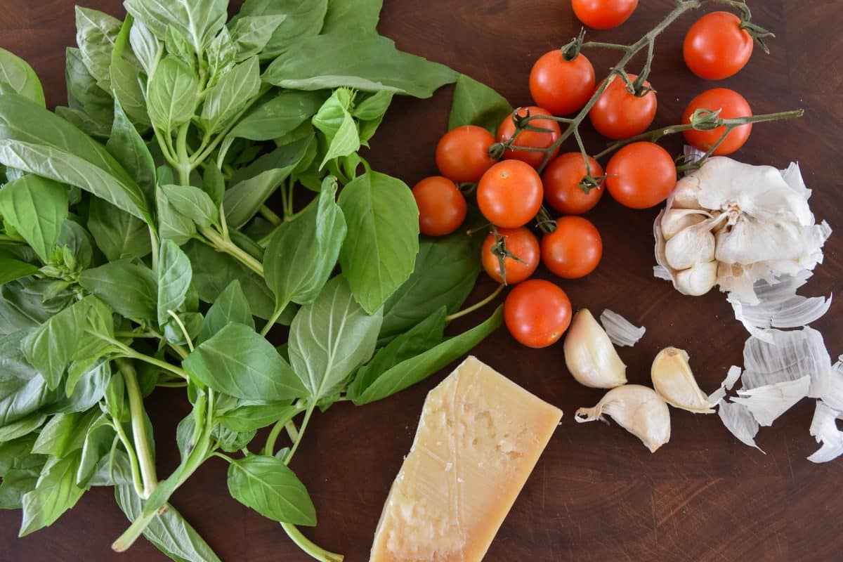bunch of fresh basil, fresh tomatoes, garlic, and parmesan cheese on a cutting board