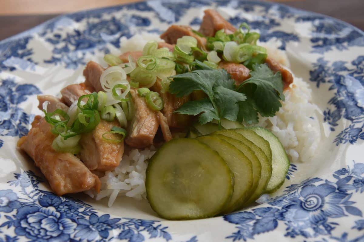 Miso chicken on a plate with rice, scallions, pickles, and cilantro .