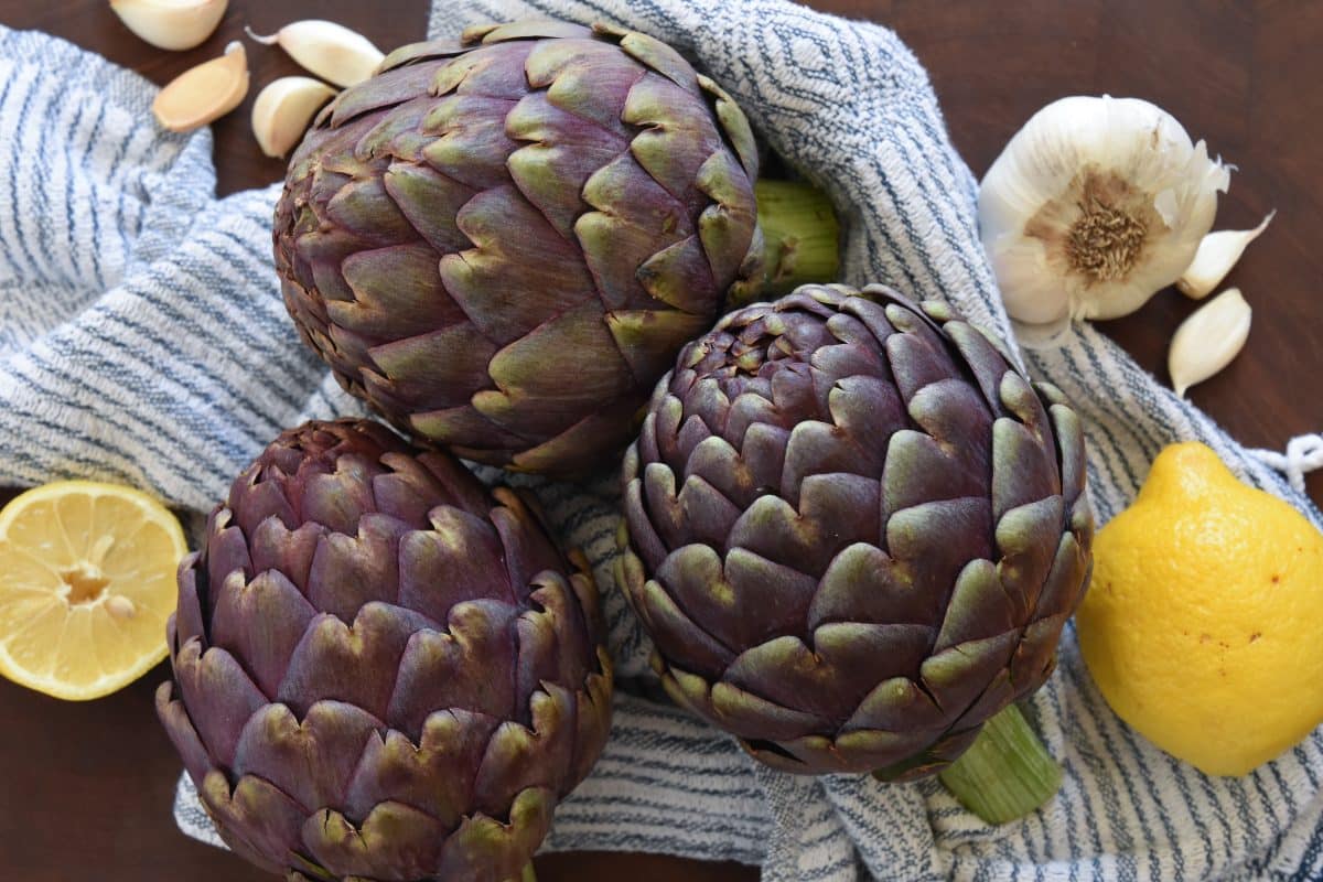 Whole artichokes, lemons, and garlic on kitchen towel. 