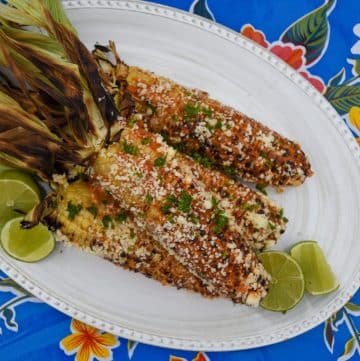 ears of chipotle grilled corn on a white platter with limes on a blue floral table cloth